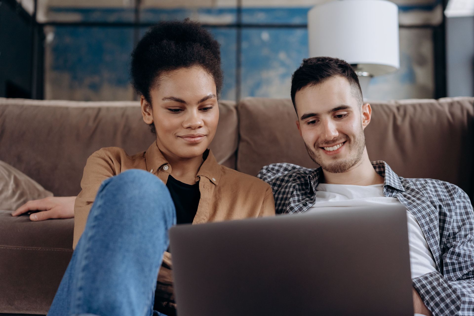 Two people smiling at a laptop on a couch in a living room