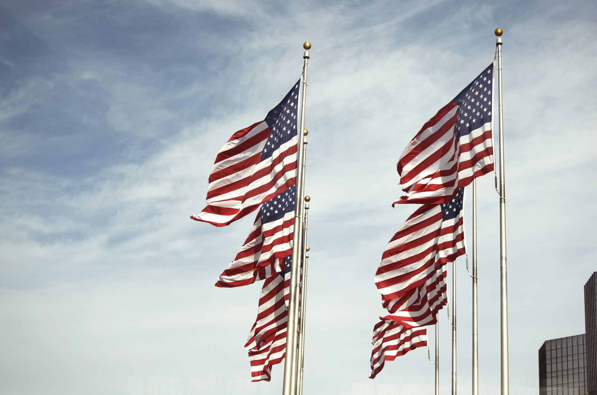 Several American flags waving on tall poles against a cloudy sky