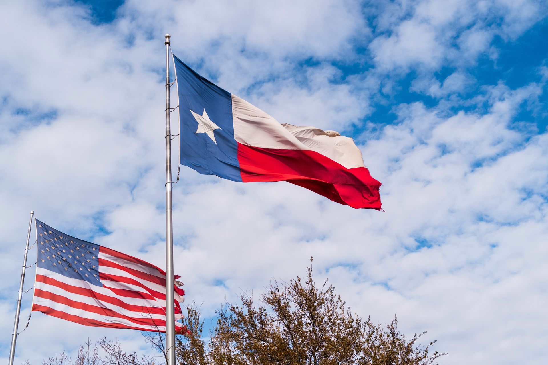 Texas and U.S. flags waving against a partly cloudy sky