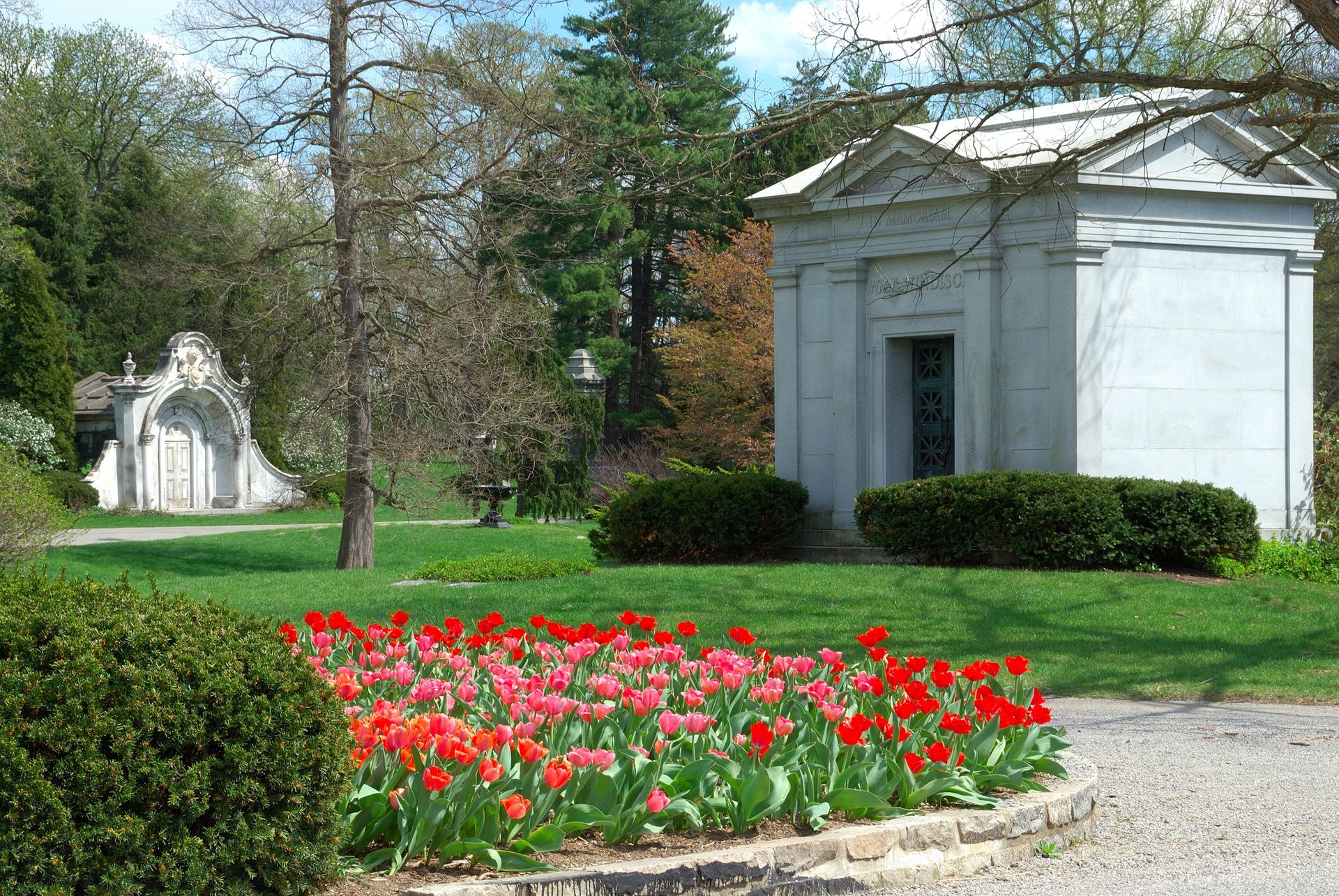 Spring cemetery with white mausoleums, green lawn, and red flowers in the foreground
