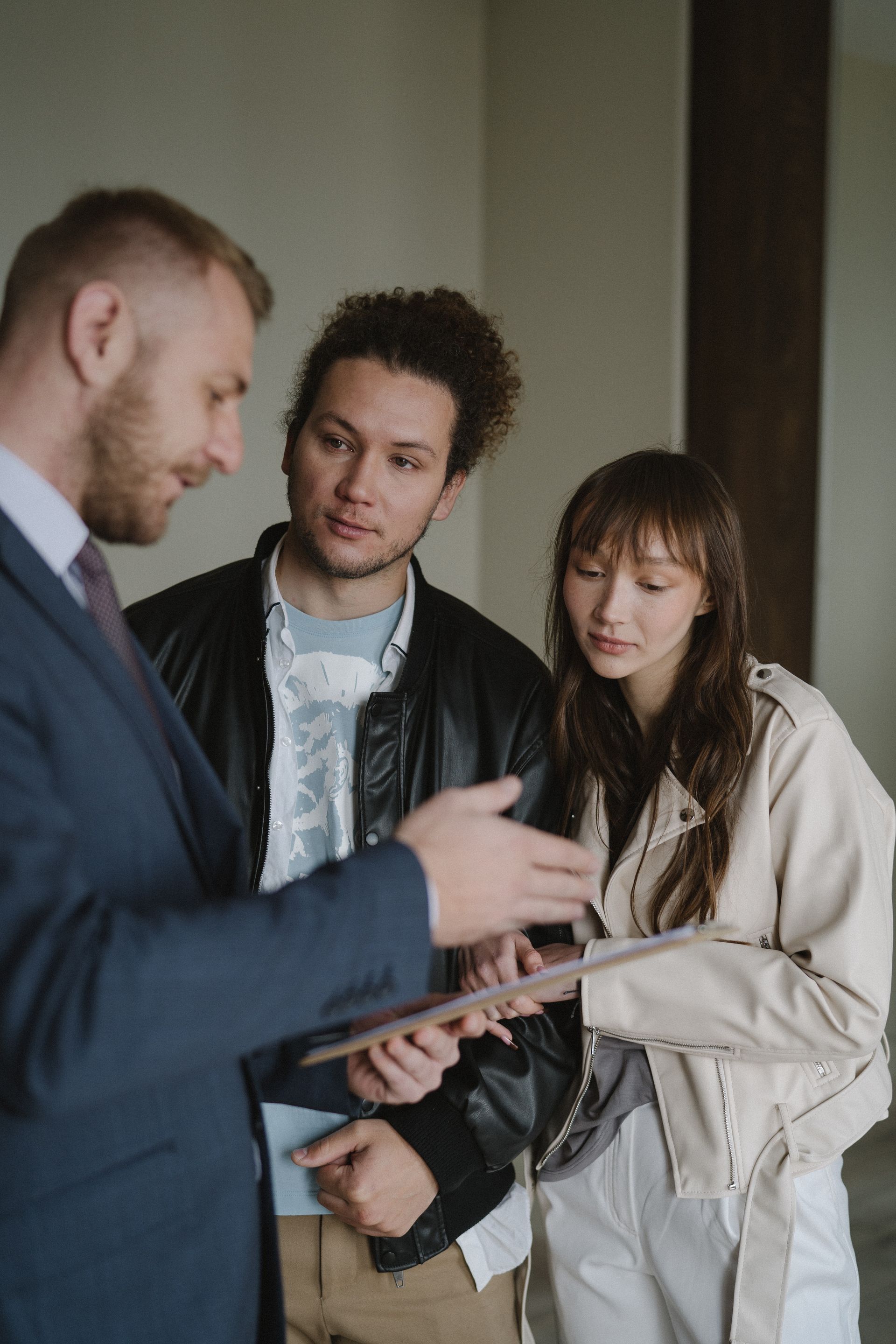 A man in a suit and tie is talking to a woman and a man in a leather jacket.