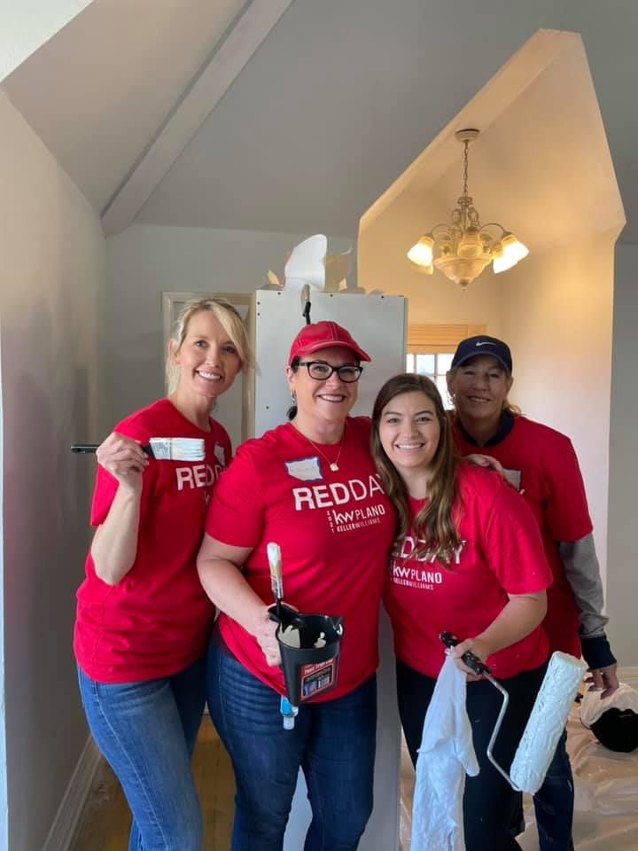 A group of people wearing red shirts are painting a wall.