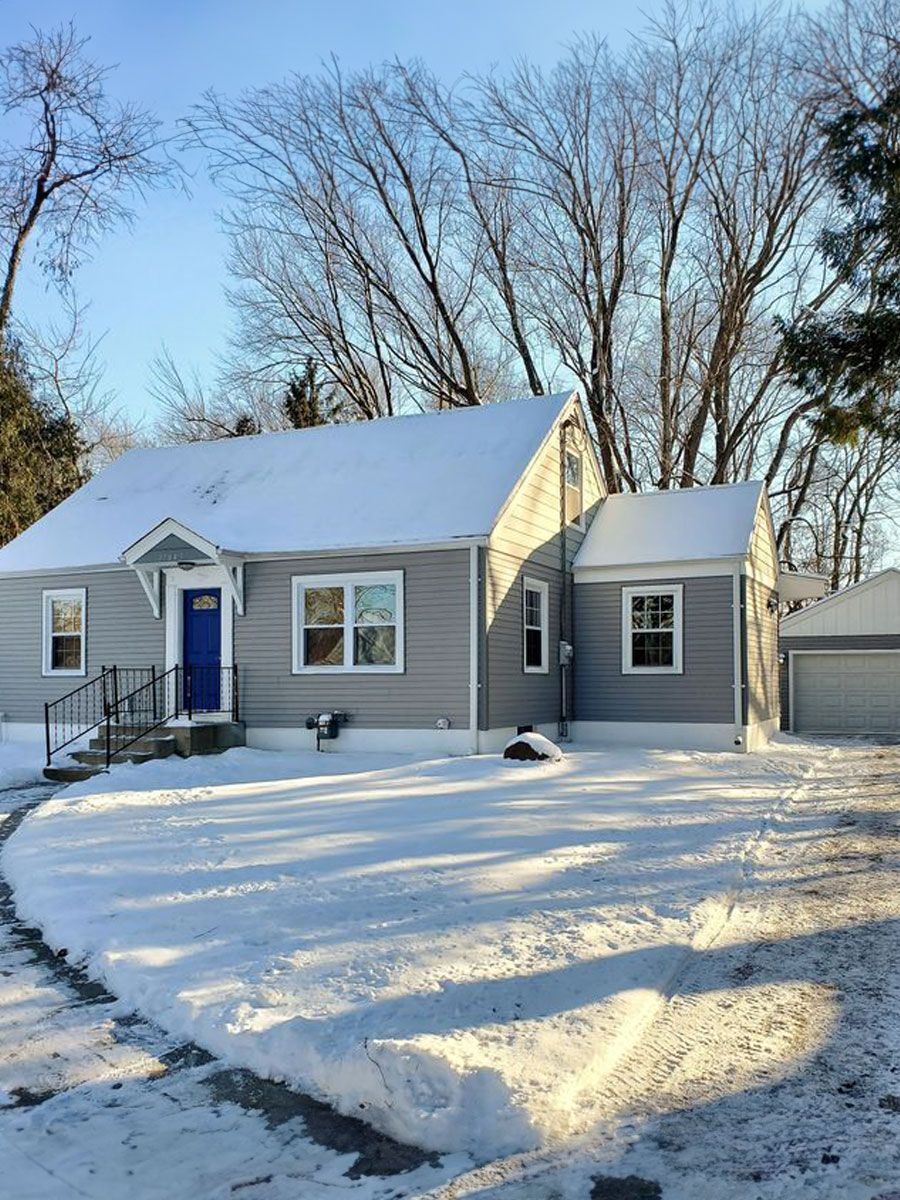 A gray house with a blue door is covered in snow.
