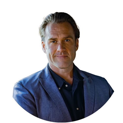 A man in a blue suit and black shirt looks at the camera