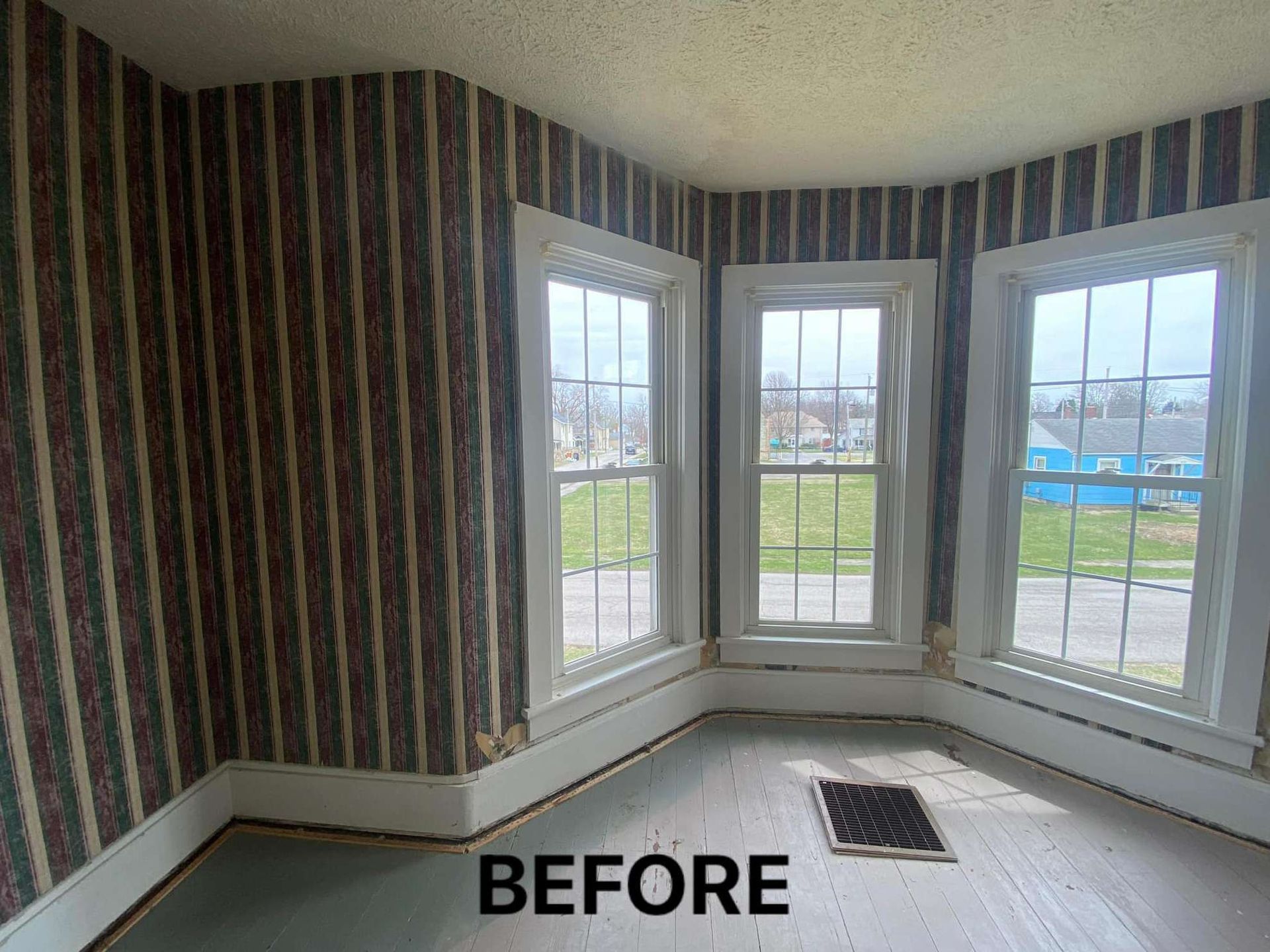 A before picture of a room with striped wallpaper and windows