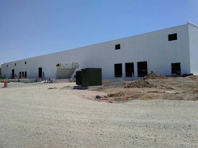 A large white building is being built on a dirt road