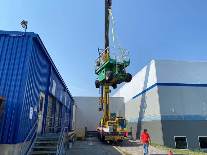 A crane is lifting a green vehicle in front of a building.