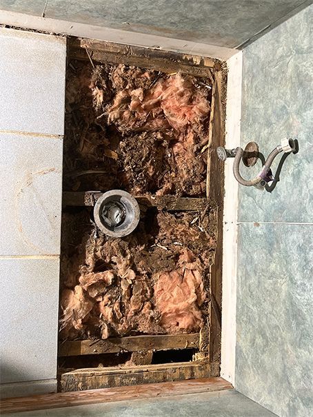 A bathroom wall with a hole in it and a shower head.