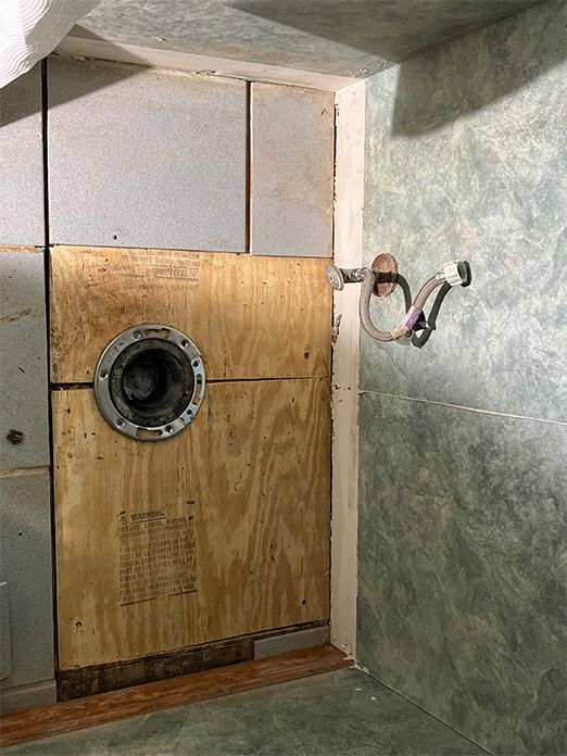 A bathroom with a wooden door and a hose hanging from the wall.