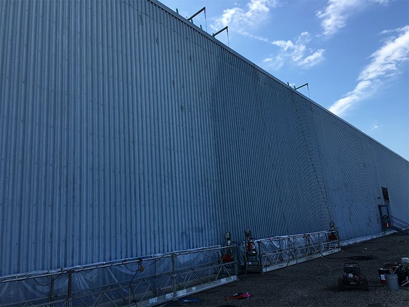 A large blue building with a blue sky in the background is being painted.