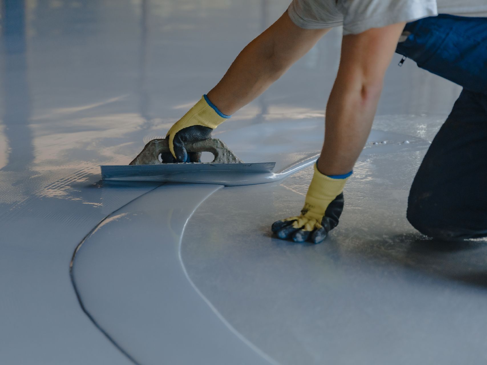 A person is using a trowel to spread concrete on a floor.