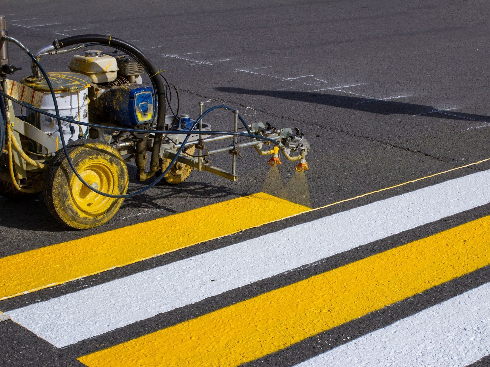 A yellow and white machine is painting a yellow line on a crosswalk.
