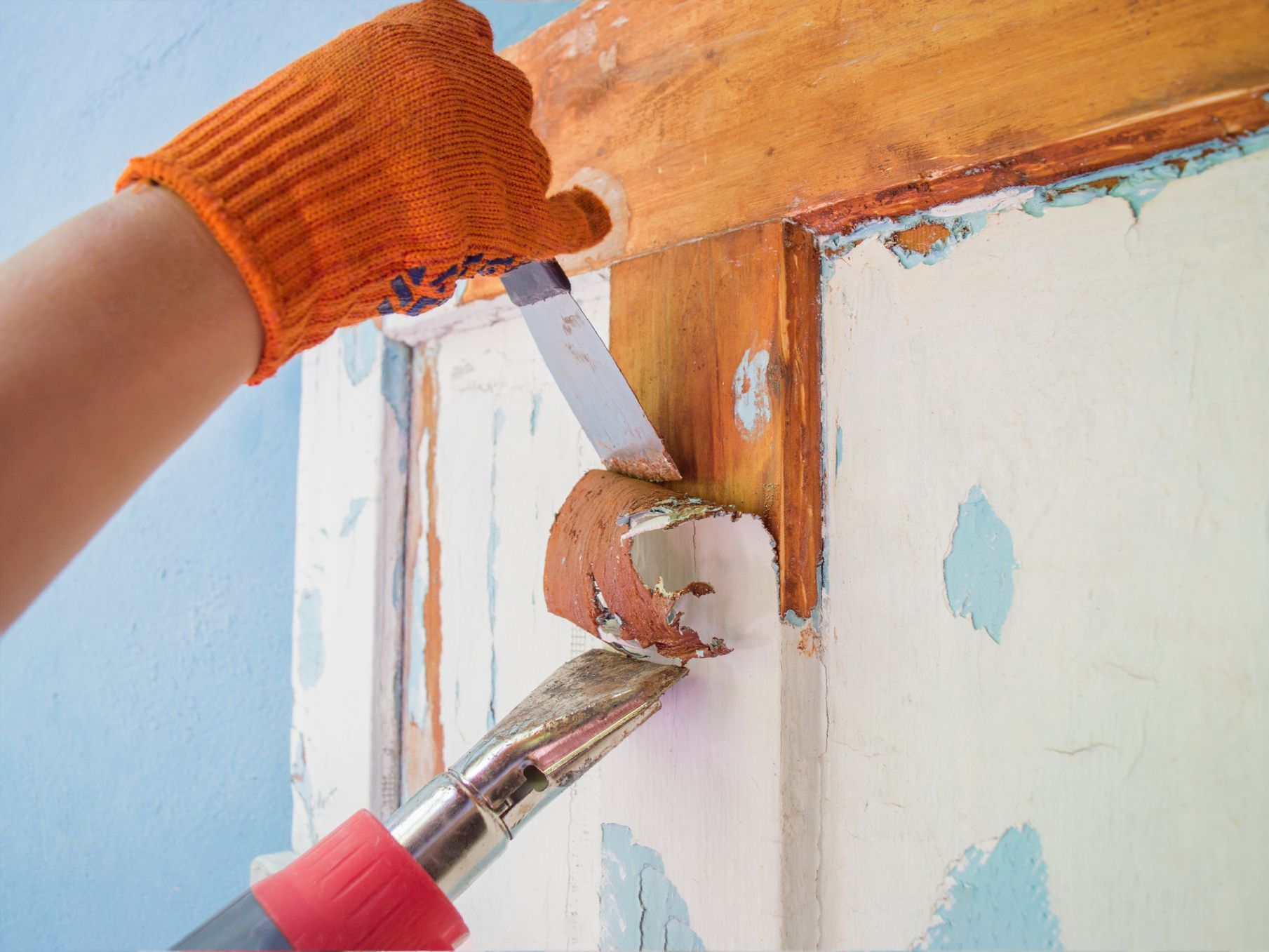 A person is using a spatula to remove paint from a door.