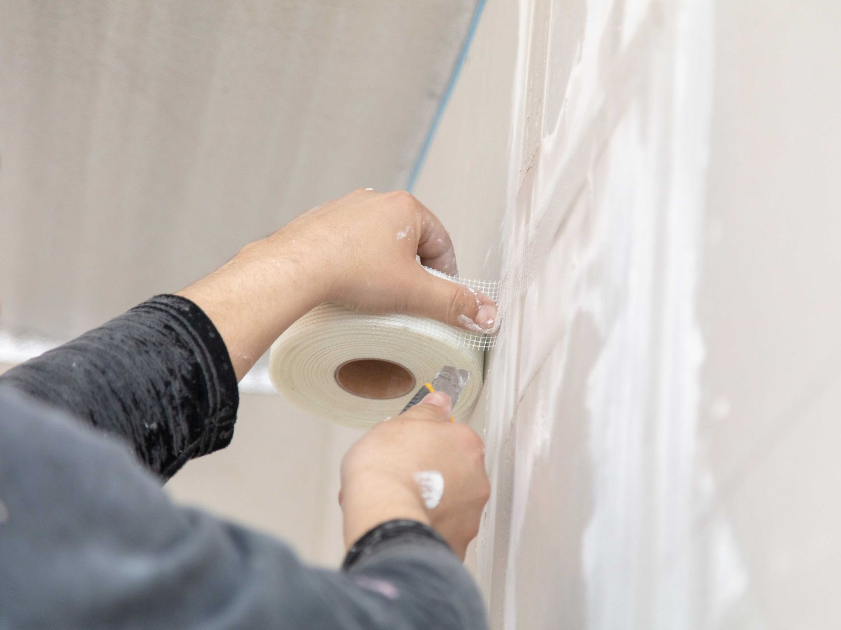 A person is cutting a piece of tape on a wall.