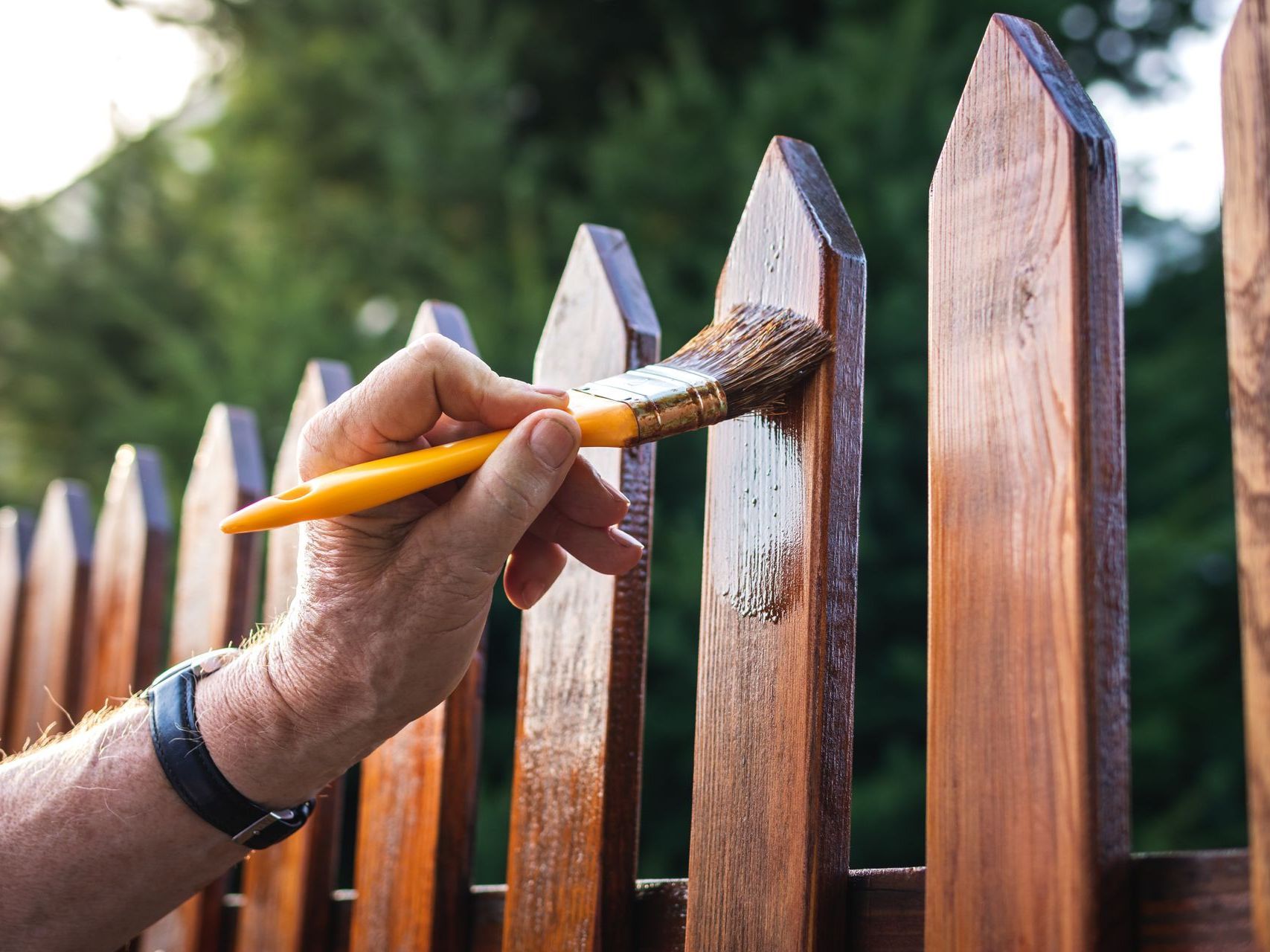 A person is painting a wooden fence with a brush.