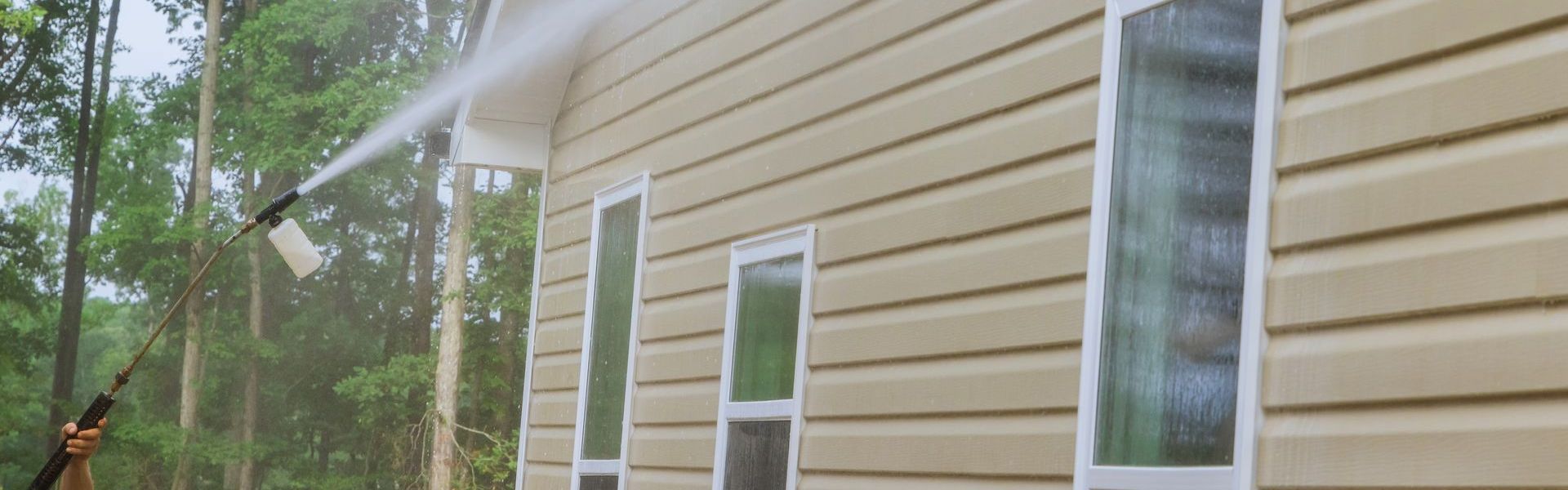 A man is using a high pressure washer to clean the side of a house.