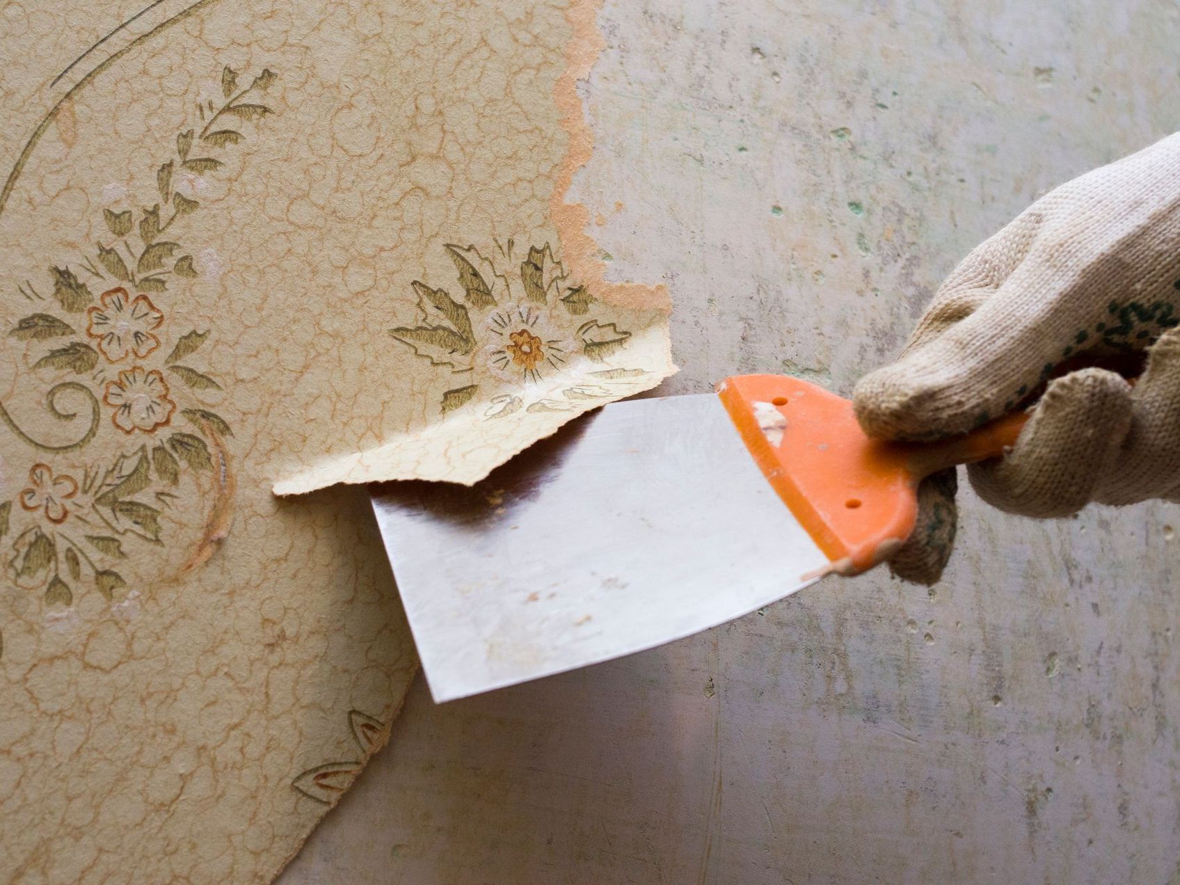 A person is removing wallpaper from a wall with a spatula.