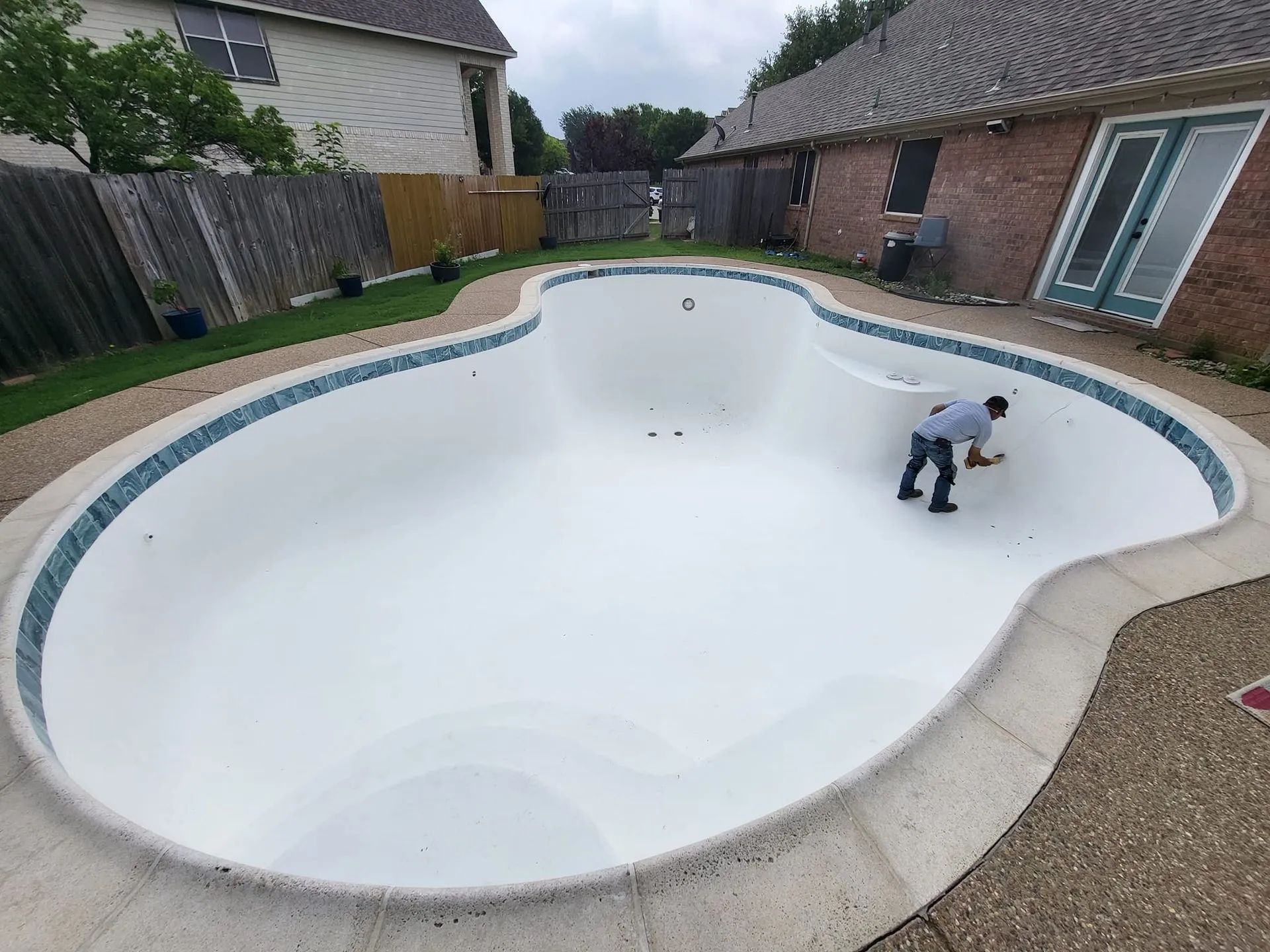Empty backyard swimming pool being cleaned by a person near the deep end
