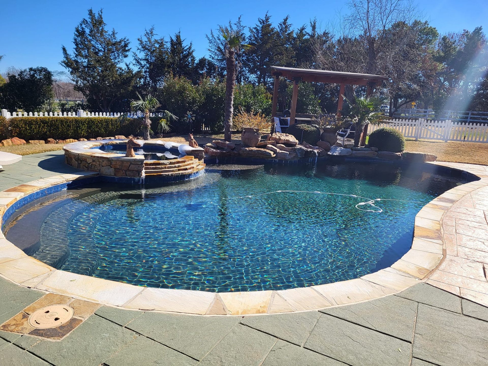 Swimming pool with rock features and a pergola in a sunny outdoor setting.