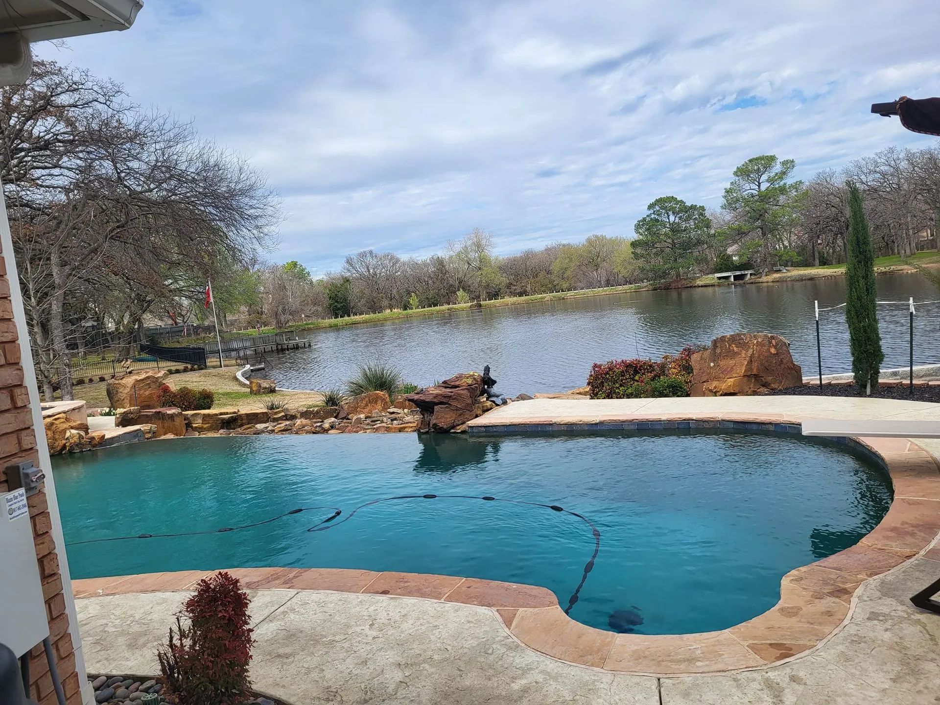 A pool overlooks a lake on a sunny day. Brown rocks and plants surround the pool.