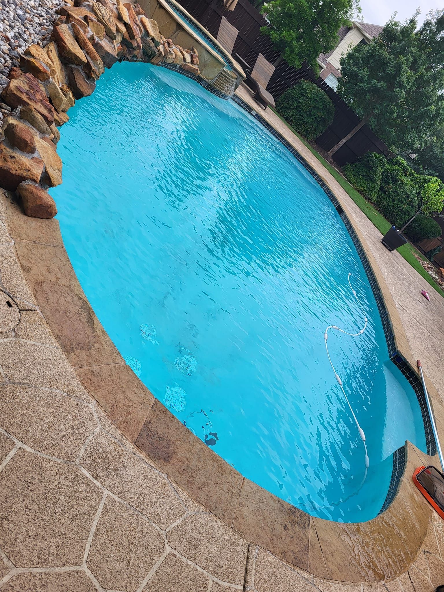 Pool with turquoise water surrounded by a stone patio. Decorative rock border along one side. 
