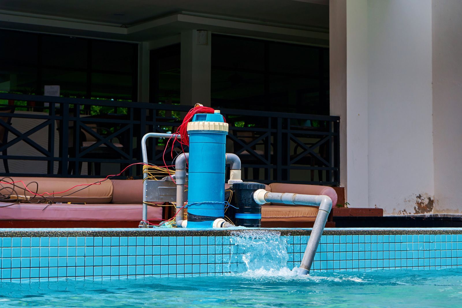 Blue pool pump and pipe spraying water into a swimming pool beside a tiled deck