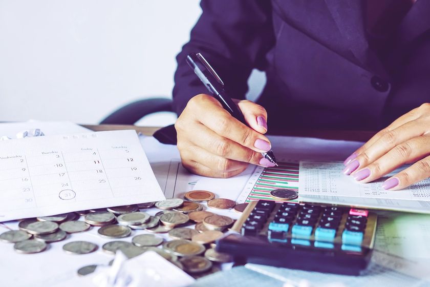 A woman is sitting at a table using a calculator and writing on a piece of paper.