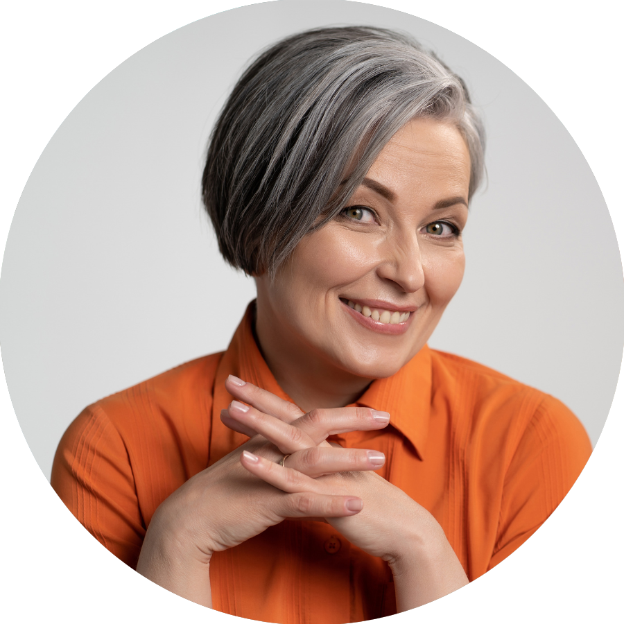 A woman with gray hair is wearing an orange shirt and smiling.