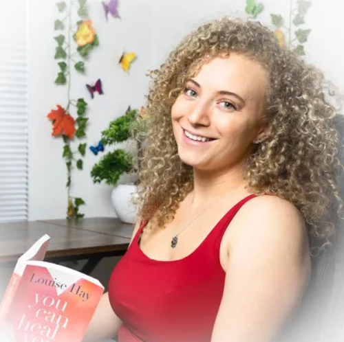 A woman in a red tank top is holding a book by louise may