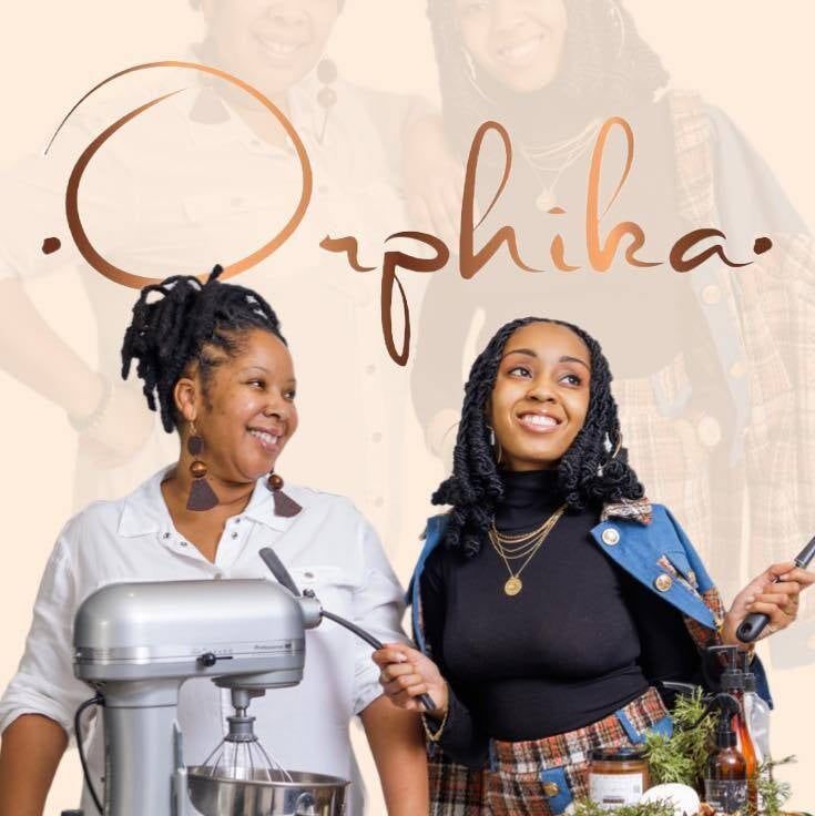 Two women standing next to a mixer with the word orpha on the bottom