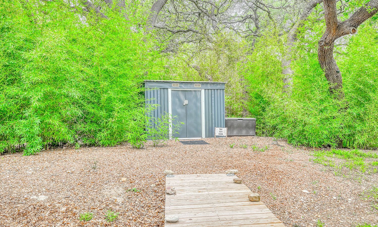 A wooden walkway leading to a shed surrounded by trees and bushes.