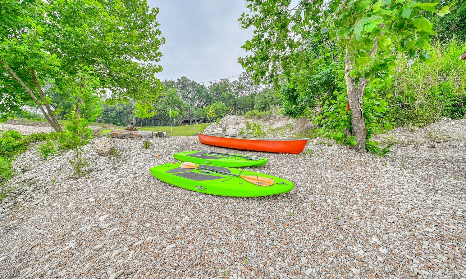 Two green kayaks and an orange canoe are sitting on a pile of gravel.