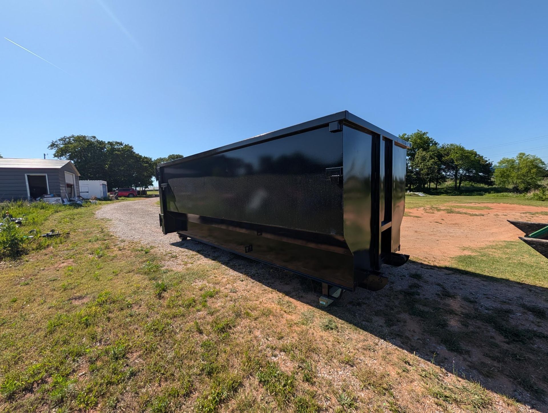 Black enclosed utility trailer parked on grass under a clear blue sky.