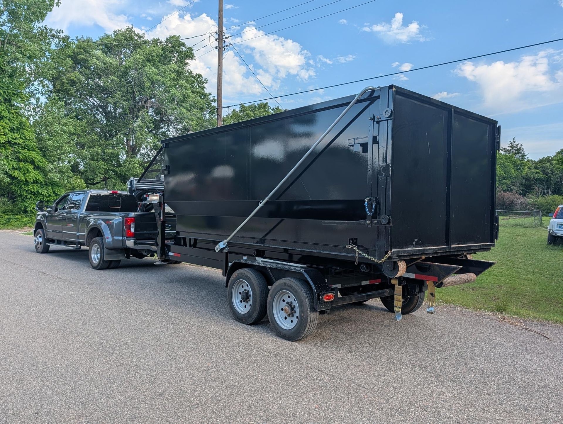 Black enclosed trailer hitched to a pickup truck on a gravel roadside under a blue sky