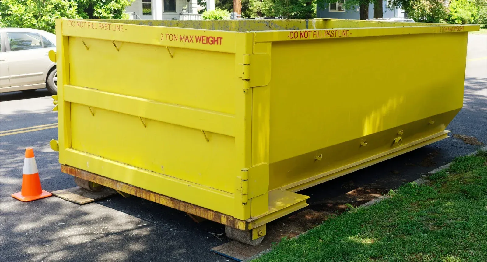 Yellow dumpster on wheels parked next to a green lawn and a street with a car.