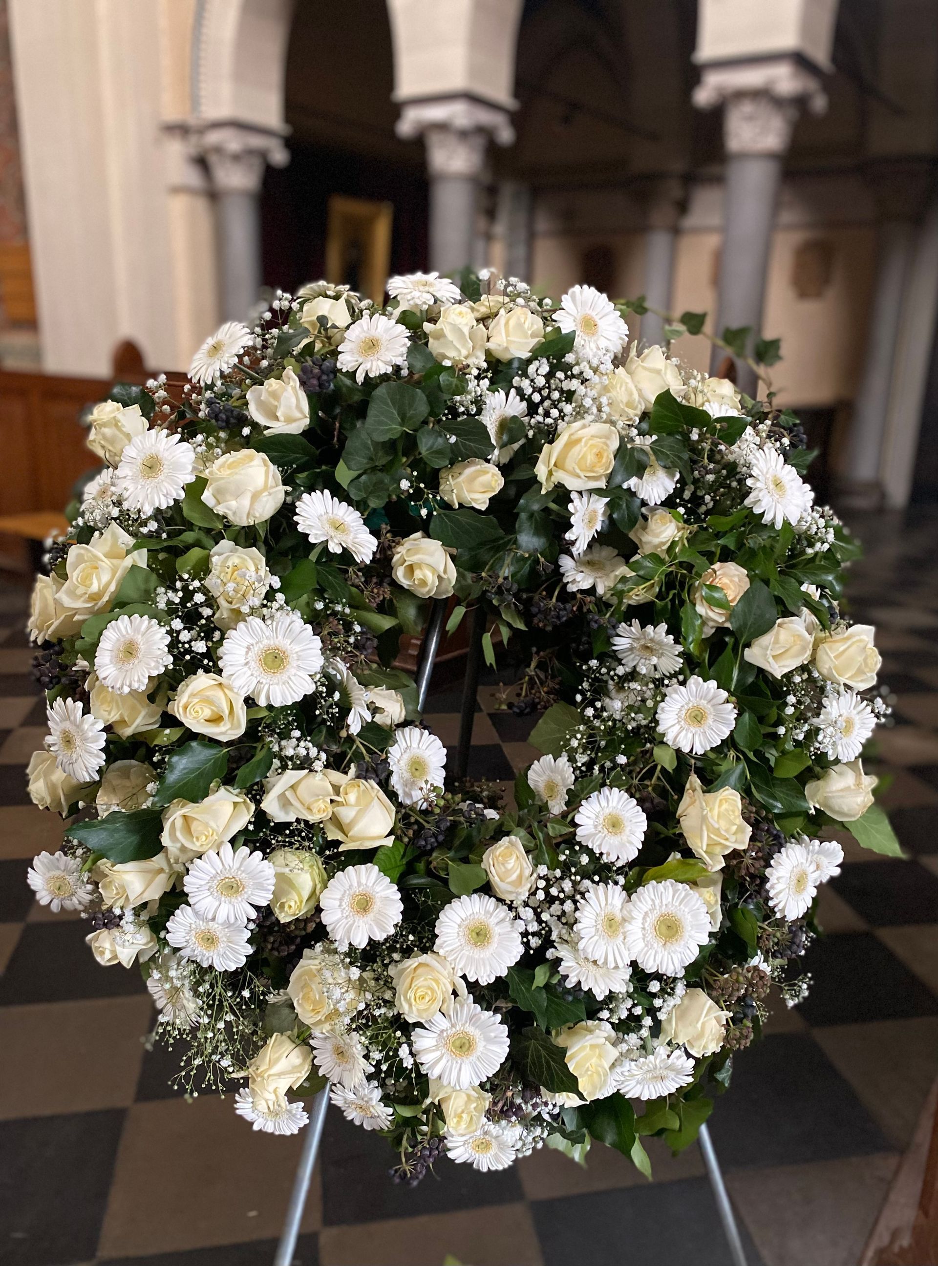 Vor einer Backsteinmauer steht ein Kranz aus gelben und weißen Blumen.