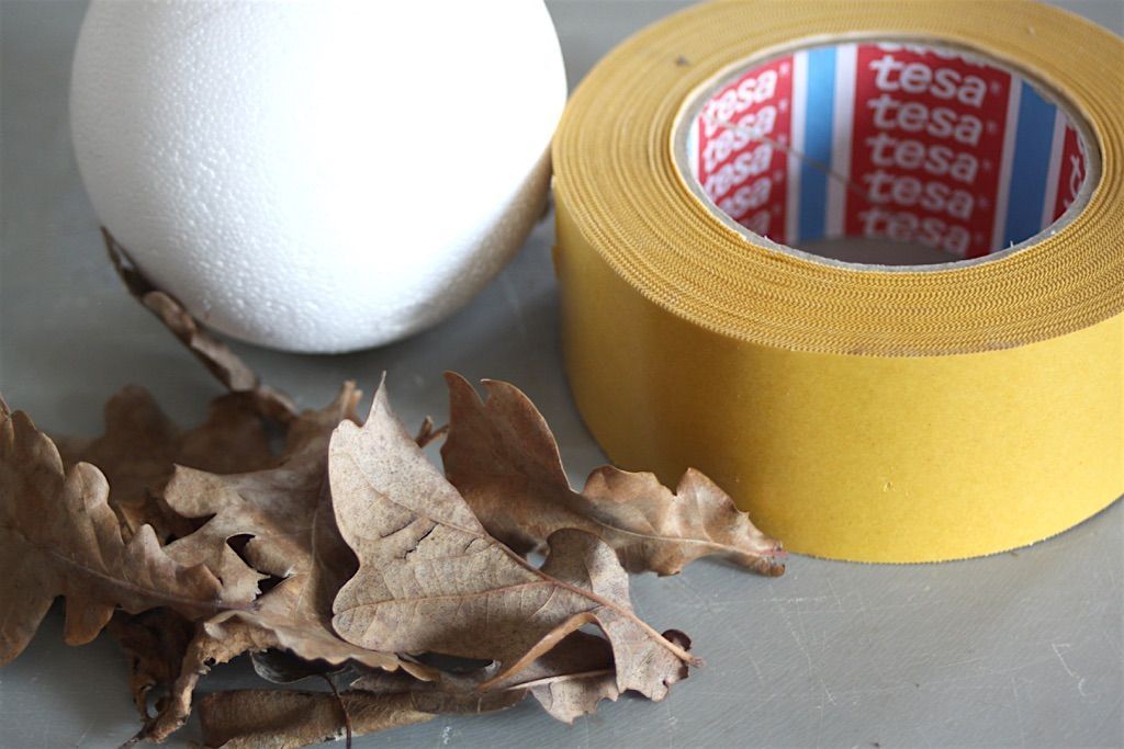 Eine Rolle Tesa-Klebeband neben einigen Blättern und einer Styropor Kugel