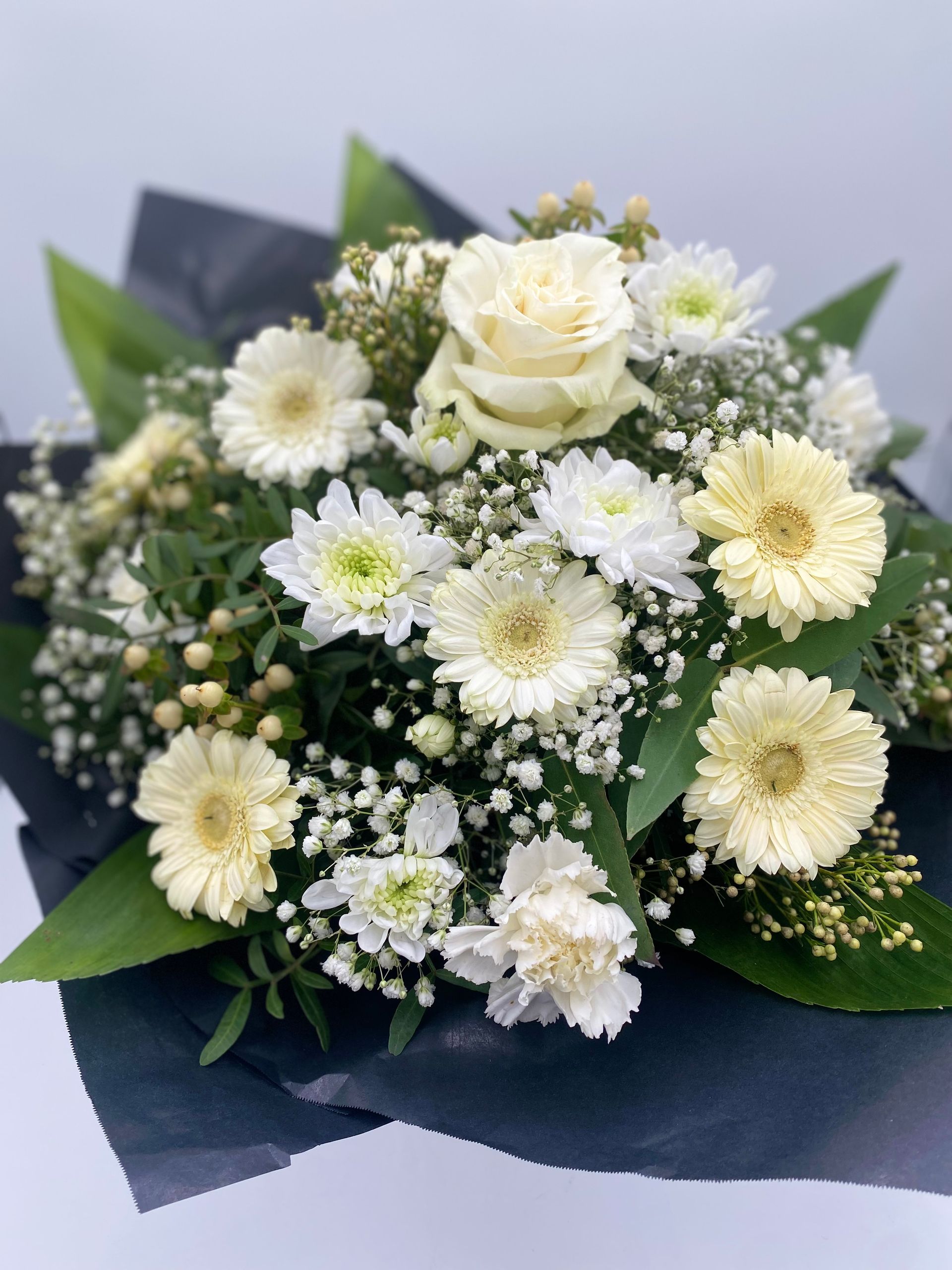 Ein Strauß weißer Blumen, eingewickelt in schwarzes Papier, auf einem Tisch.