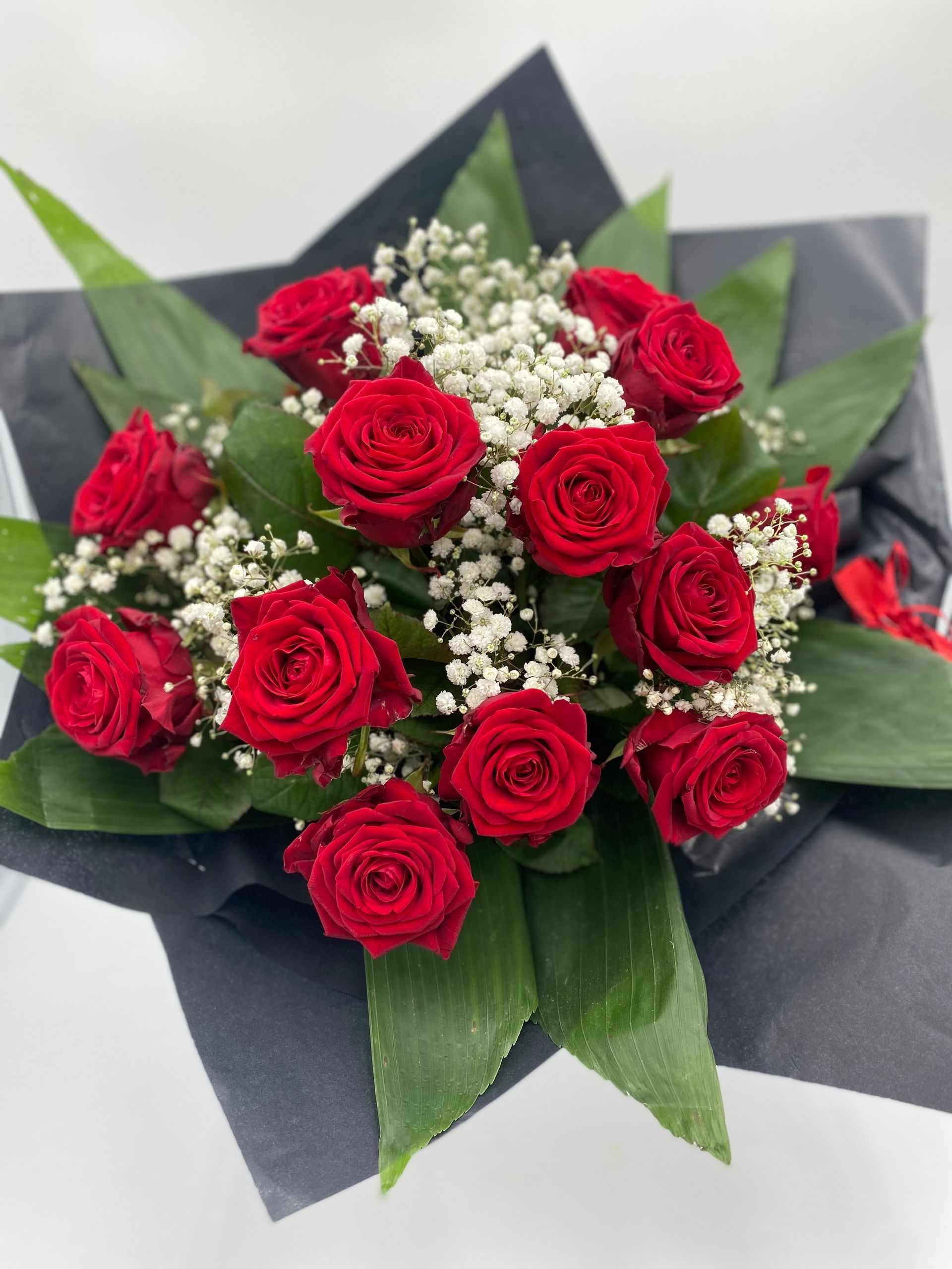 Ein Strauß roter Rosen und Schleierkraut in schwarzes Papier gewickelt