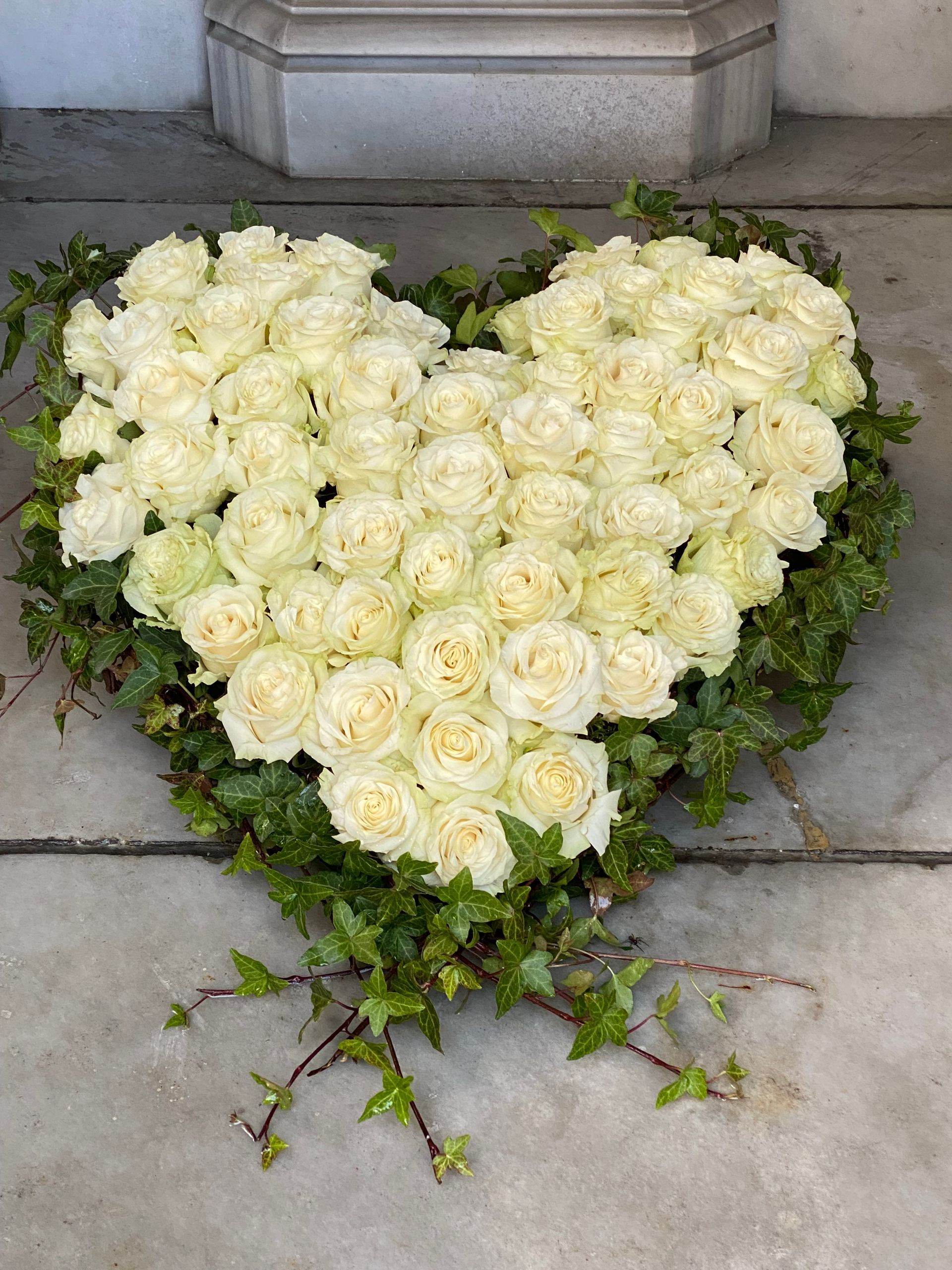 Auf dem Boden liegt ein Herz aus weißen Rosen und Efeu.