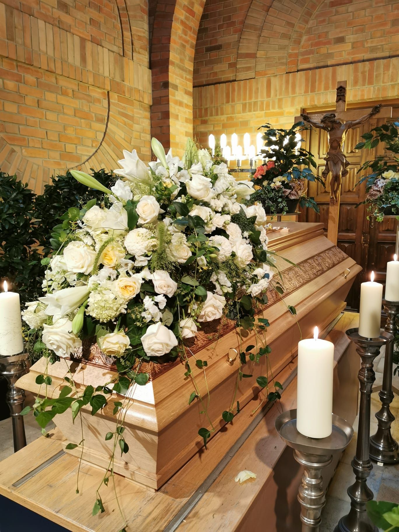 In einer Kirche ist ein Sarg von Kerzen und Blumen umgeben.