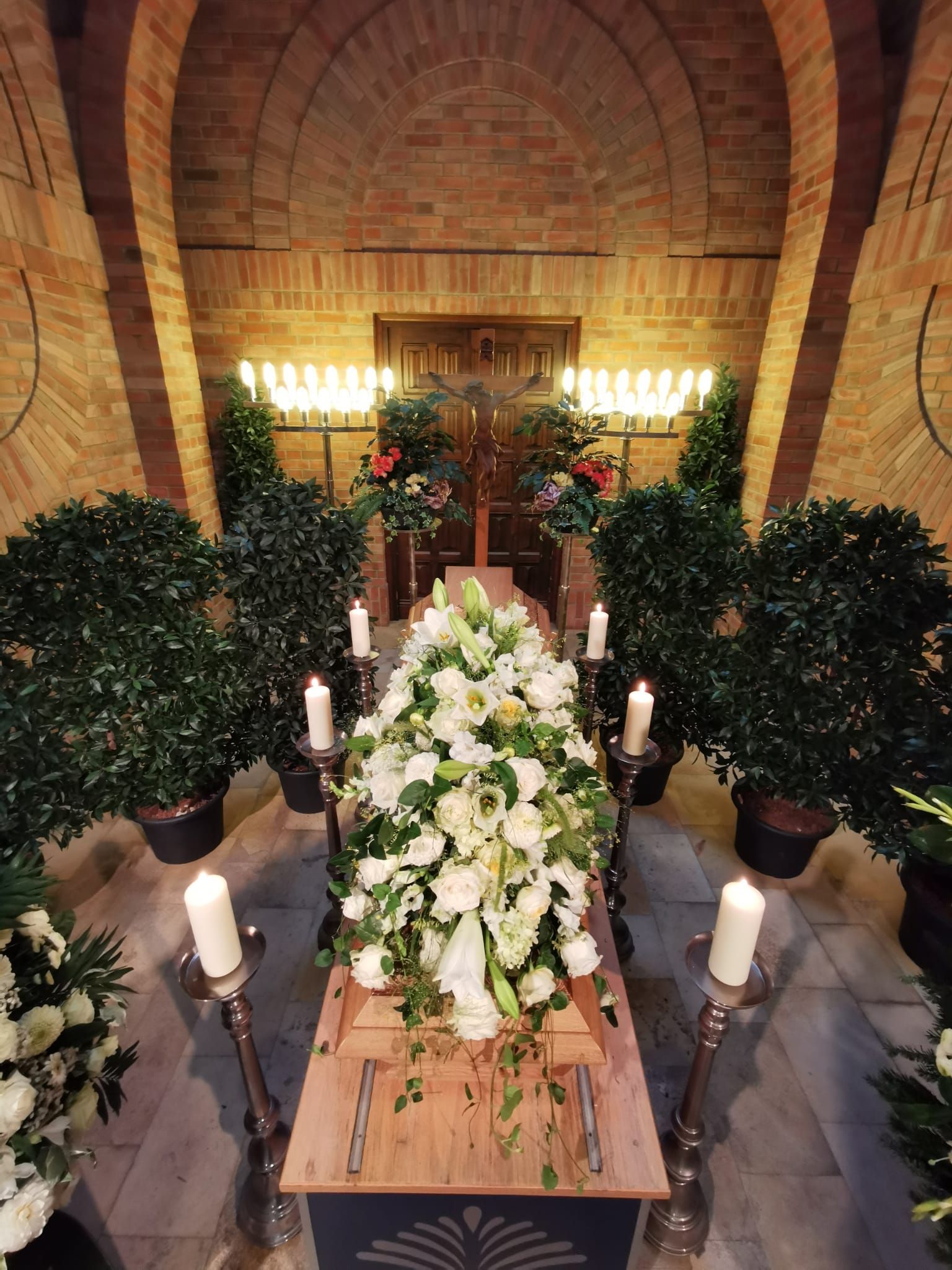 In einer Kirche ist ein Sarg mit weißen Blumen und Kerzen geschmückt.