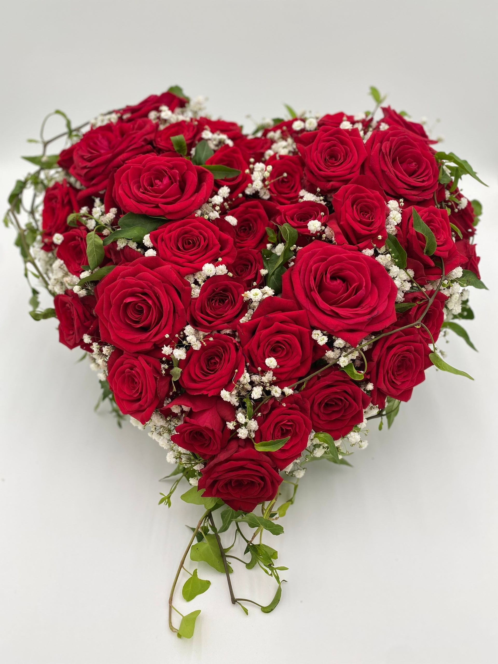 Herz aus roten Rosen auf weißem Hintergrund. Zwischen den Rosen ist weißes Schleierkraut und zarte Efeuranken.