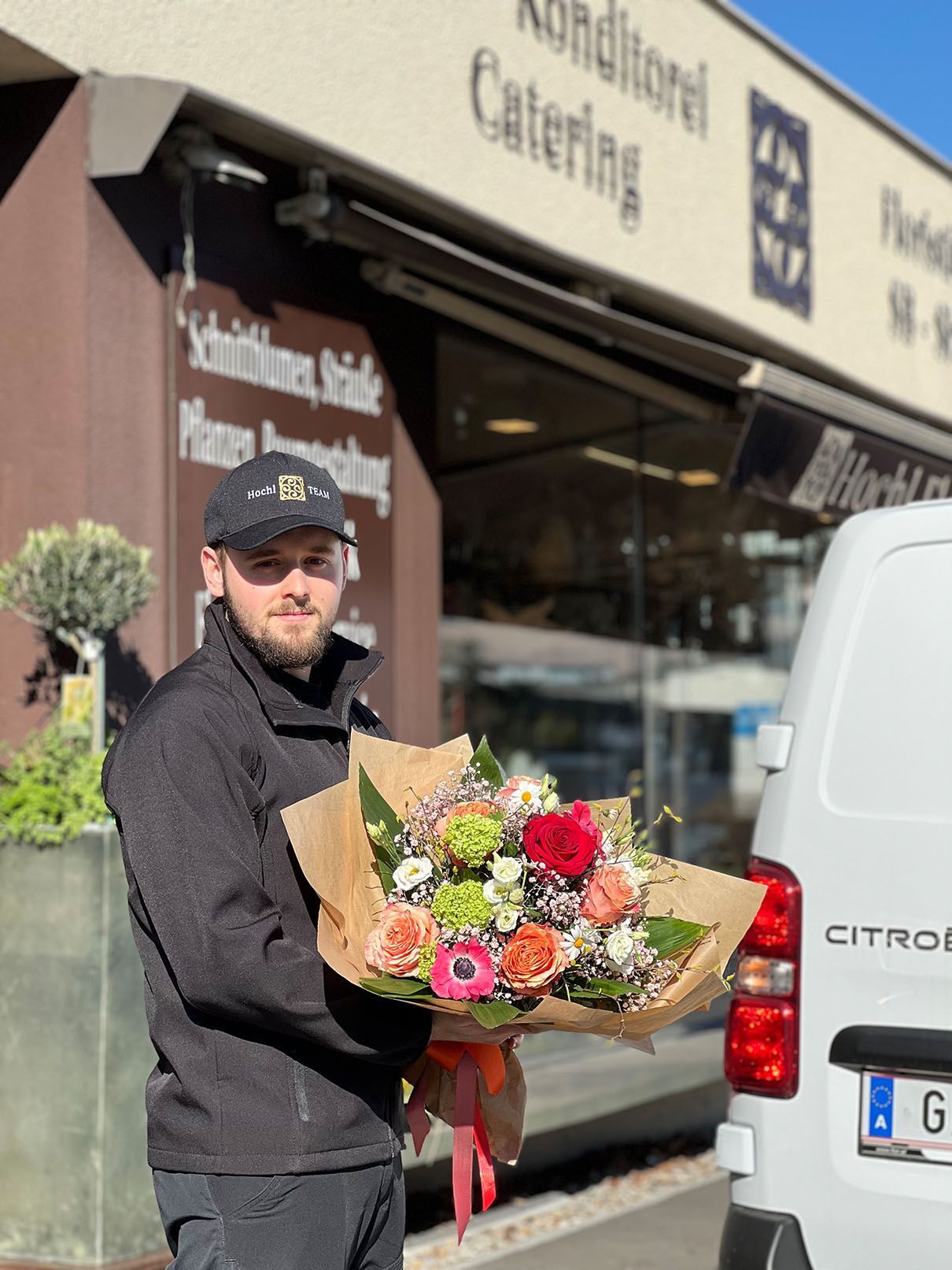 Ein Mann hält einen Blumenstrauß vor einem Citroen-Van