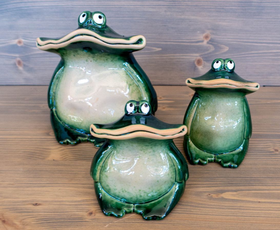 Drei grüne Froschskulpturen sitzen auf einem Holztisch.