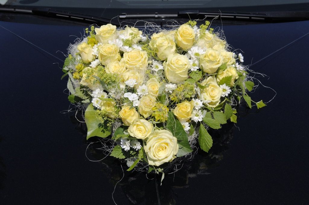 Ein herzförmiger Strauß gelber Rosen und Gänseblümchen auf der Motorhaube eines Autos.