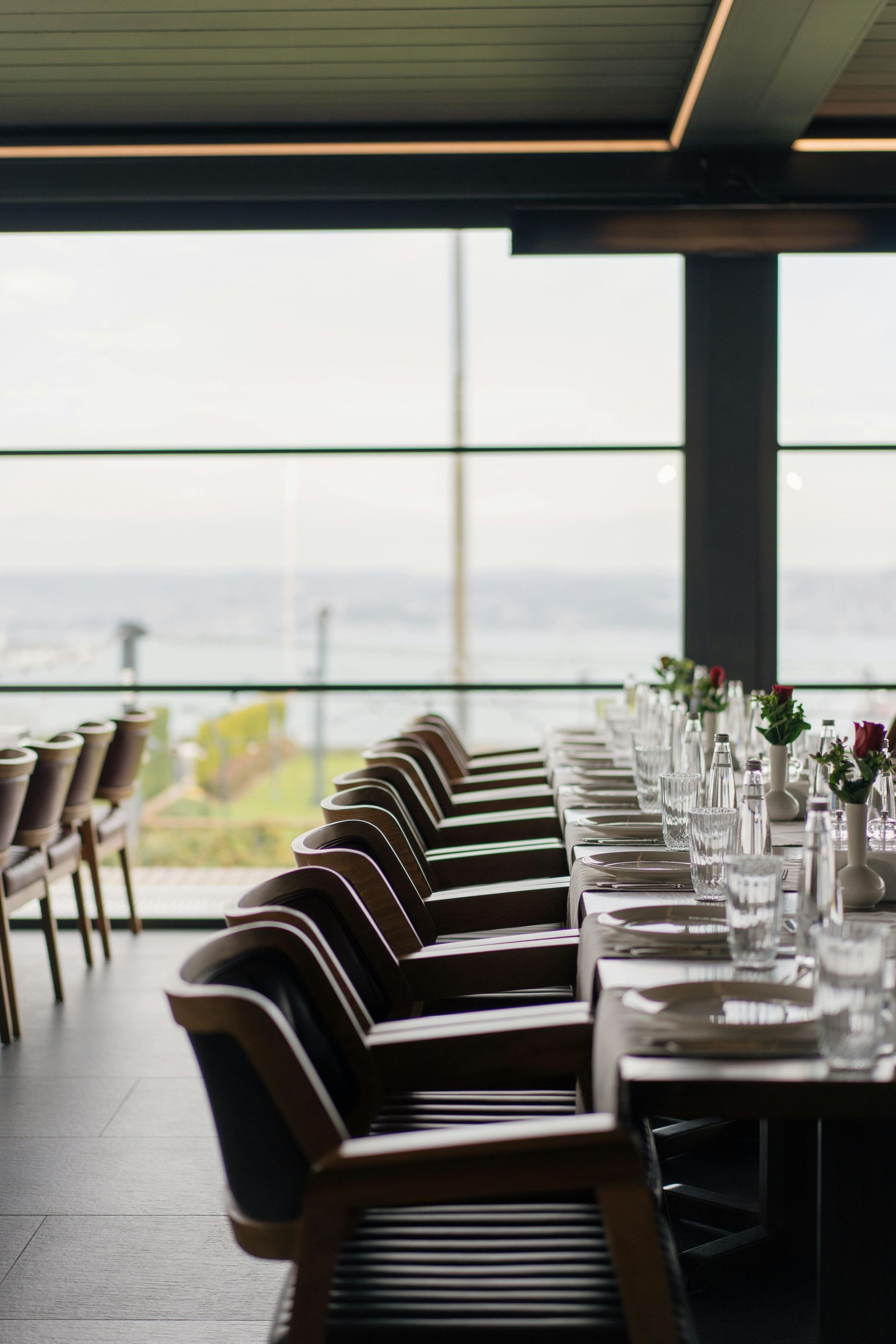 Ein langer Tisch mit Tellern und Gläsern und Blumen in einem Restaurant mit Blick aufs Meer.