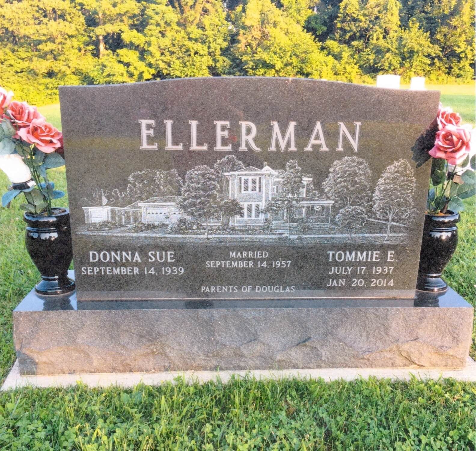 Family gravestone with engraved house, surrounded by flowers and trees