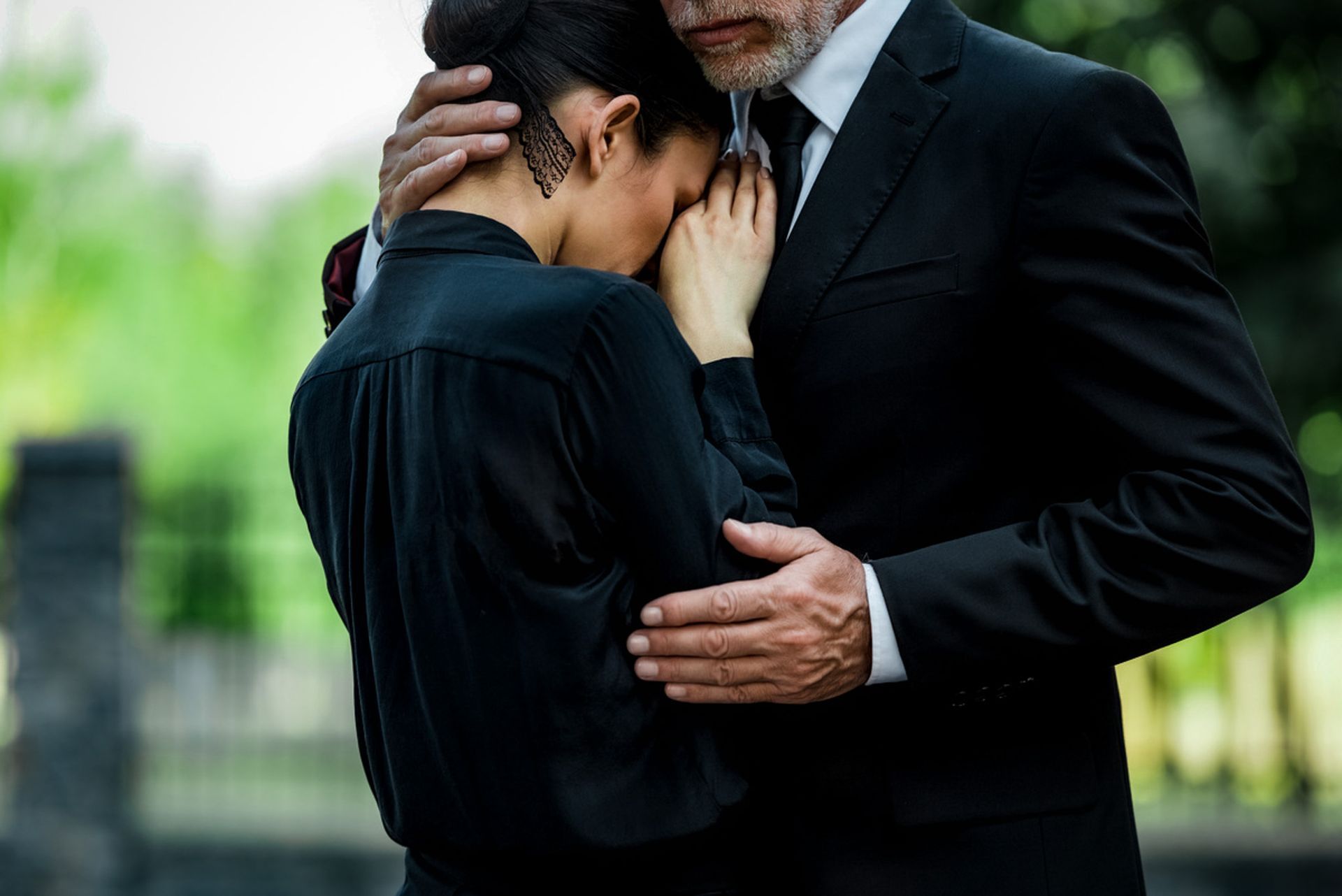 Two people in black clothing embrace closely outdoors, one comforting the other.