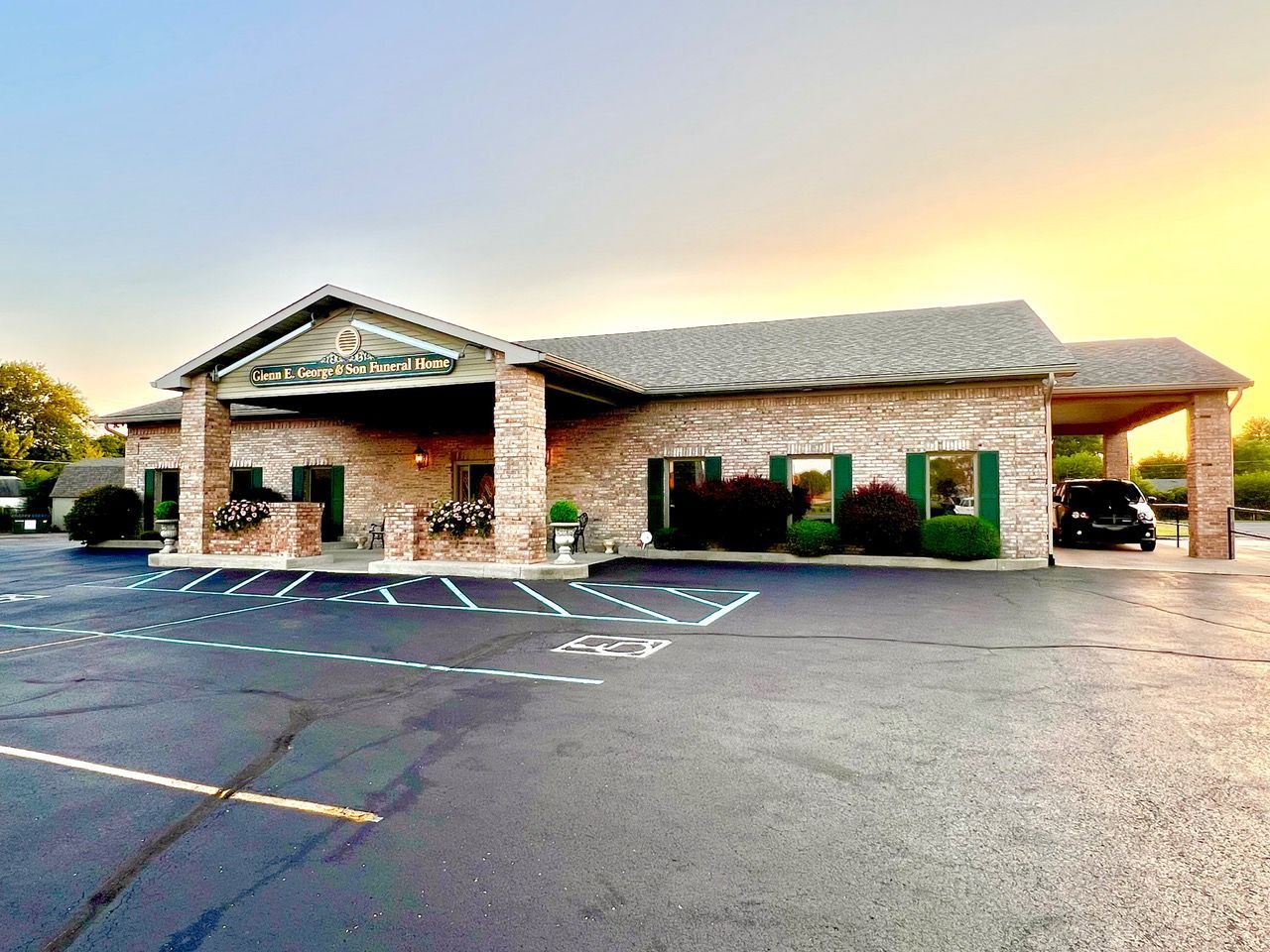 Brick office building with a covered entrance and empty parking lot at sunset